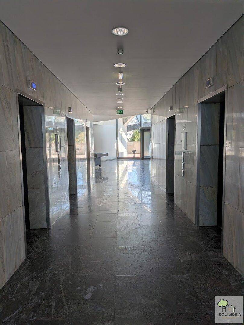Langer, heller Flur mit glänzenden Fliesen und mehreren Aufzügen in einem modernen Gebäude.