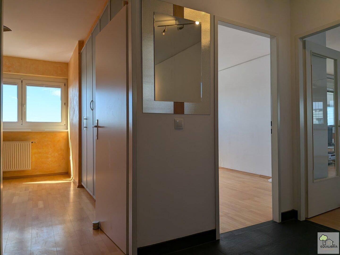 Flur mit Einbauschränken und Spiegel, bietet Zugang zu einem hellen Zimmer.