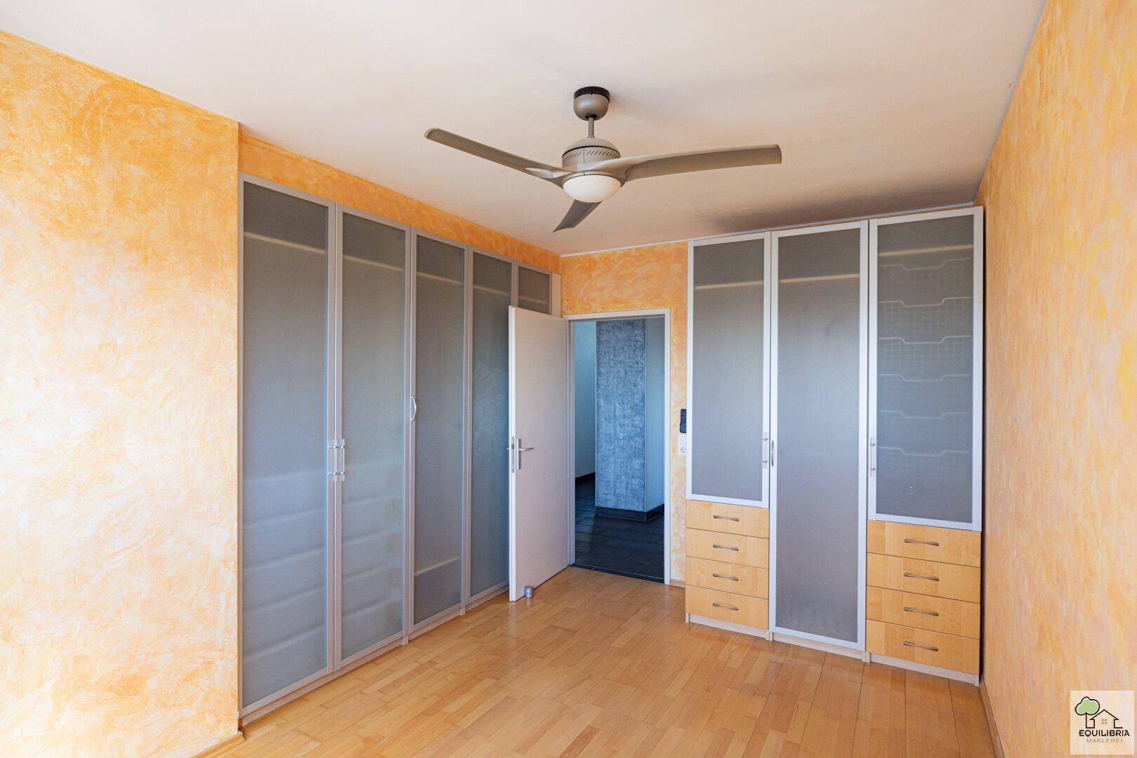 Schlafzimmer mit Einbauschränken, Deckenventilator und strukturierten Wänden.