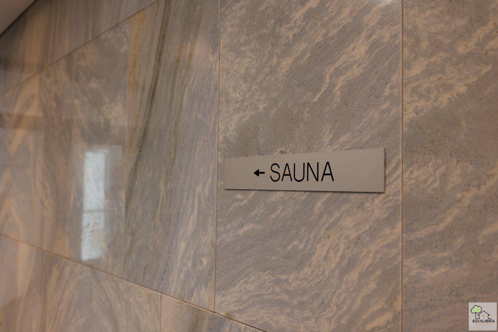 Hinweisschild zur Sauna an einer eleganten, marmorierten Wand in einem Wellnessbereich.