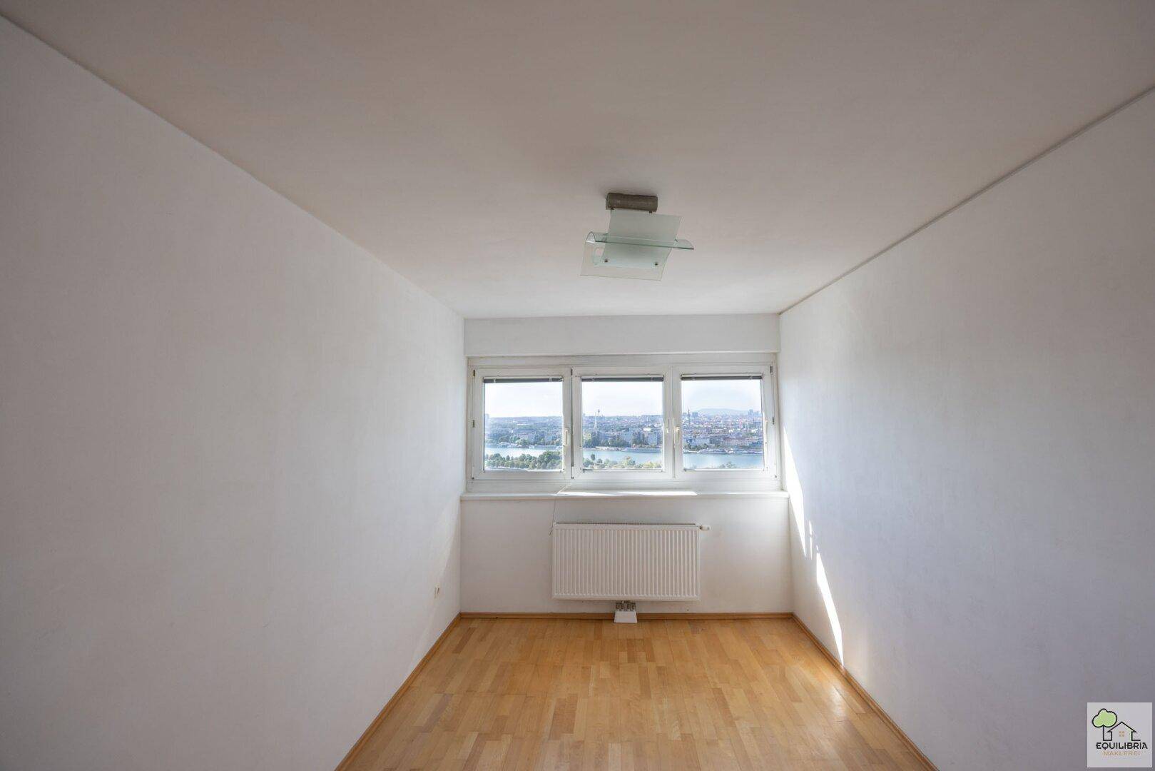Leeres Schlafzimmer mit Holzboden und Fensterfront, bietet weiten Stadtblick.