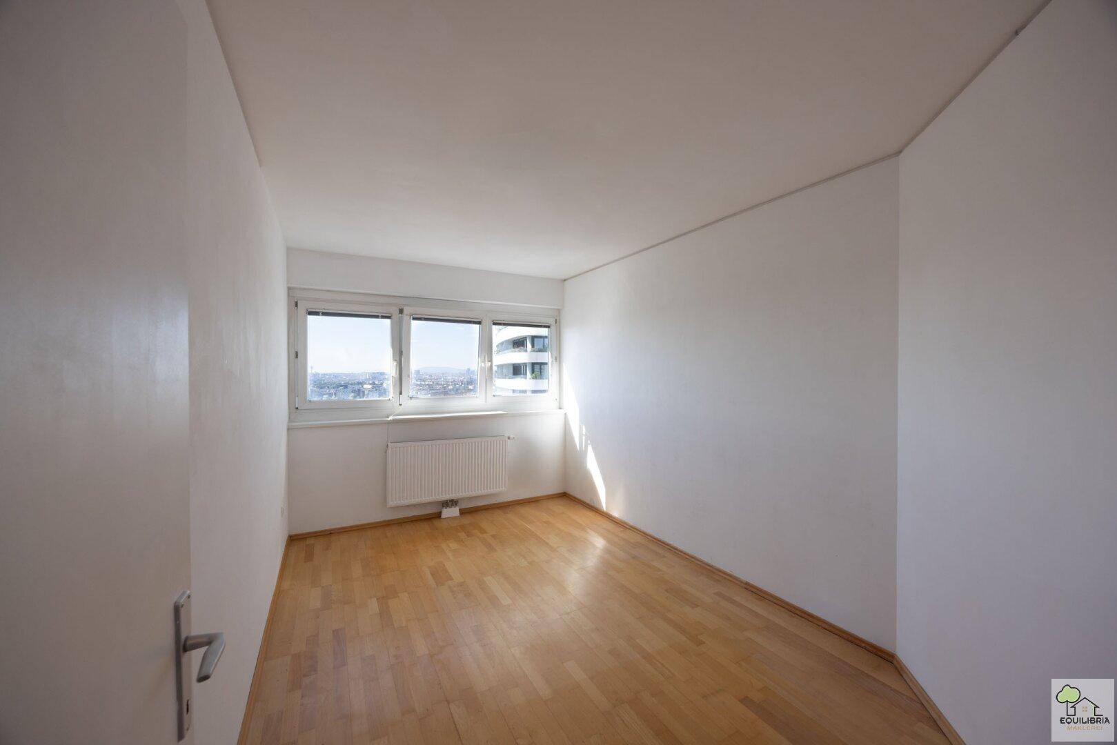 Helles Schlafzimmer mit Holzboden und Fenster, bietet weiten Blick über die Stadt.