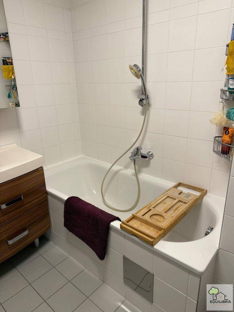 Helles Badezimmer mit Badewanne, integrierter Dusche und modernem Holzwaschtisch mit weißen Fliesen.