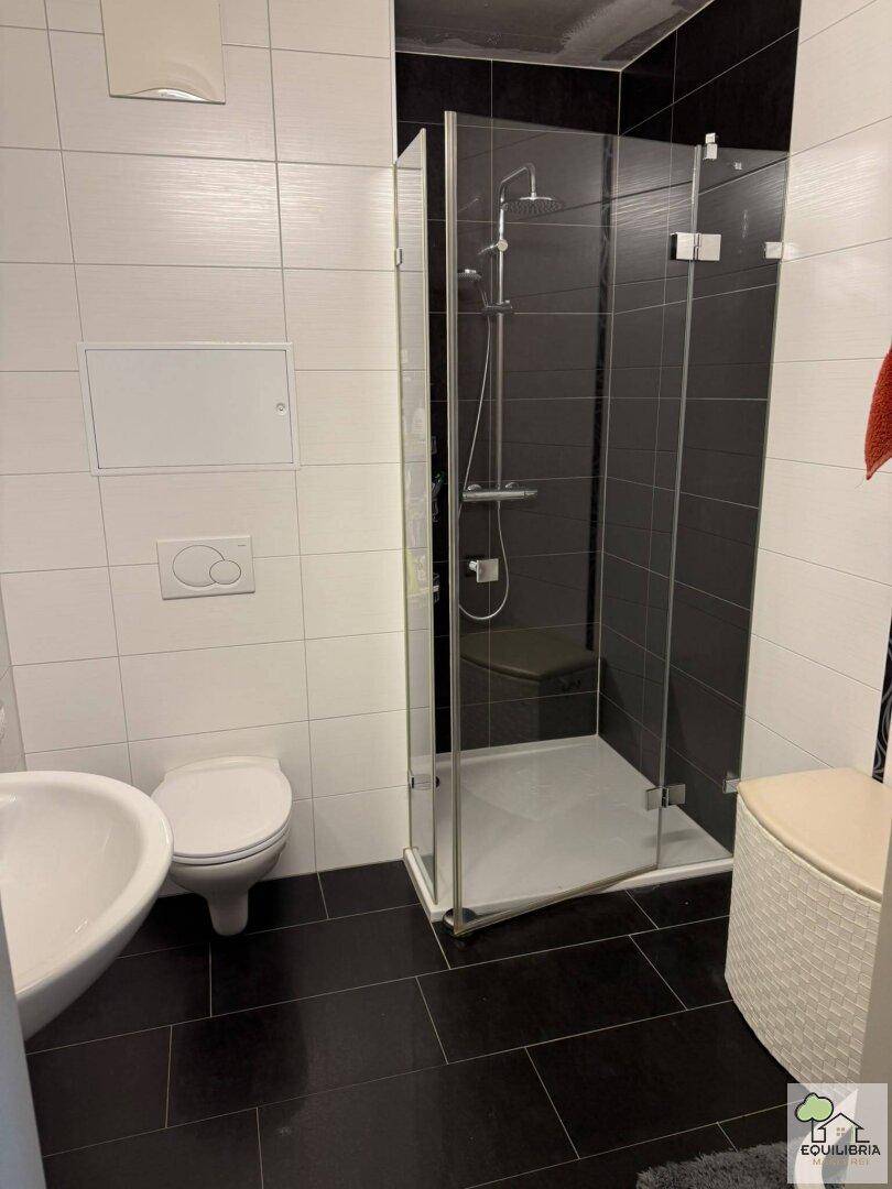 Modernes Badezimmer mit Glasduschkabine, dunklen Bodenfliesen und wandhängendem WC.