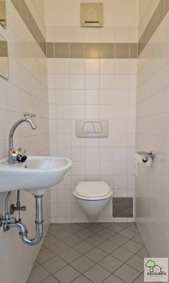 Separate Toilette mit Wand-WC, Waschbecken und weißen Fliesen.