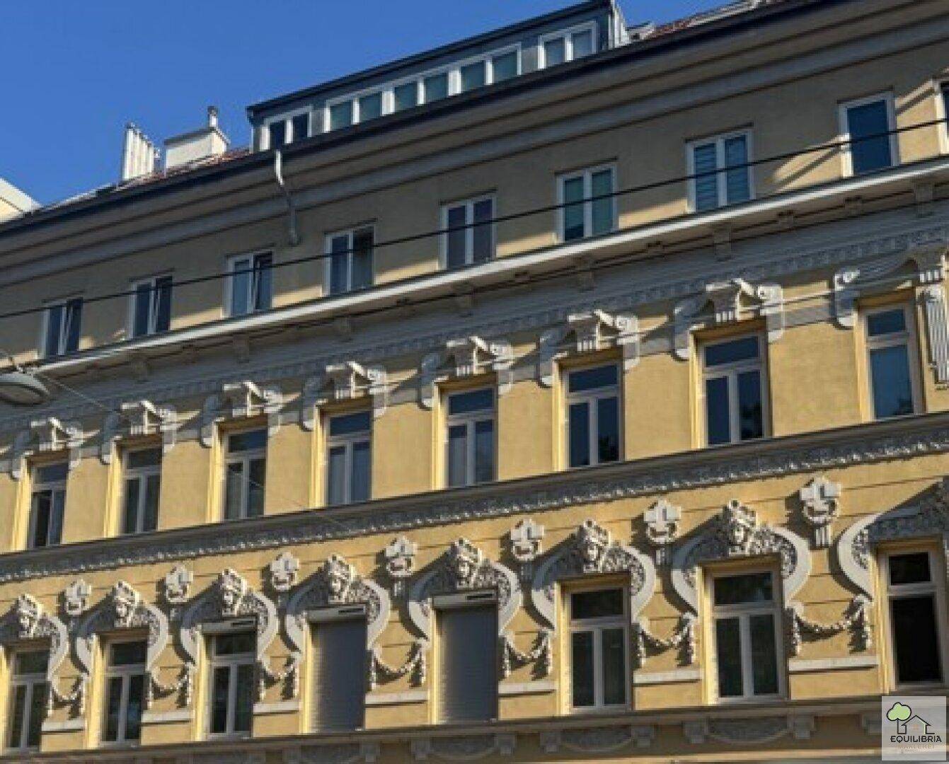 Historische Fassade eines Wohngebäudes mit dekorativen Elementen und vielen Fenstern.