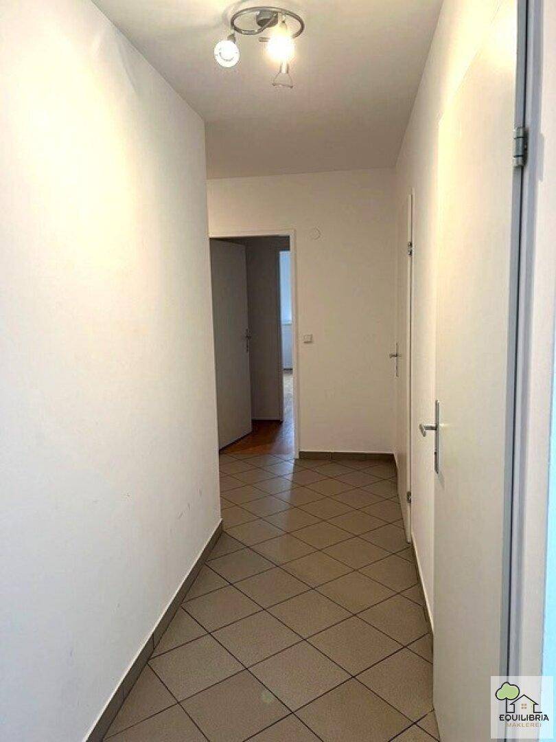 Langer Flur mit Fliesenboden und Deckenleuchte, der verschiedene Bereiche verbindet.