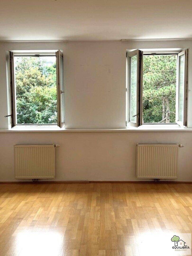 Zwei Fenster in einem hellen Raum mit Parkettboden und Blick auf Bäume.