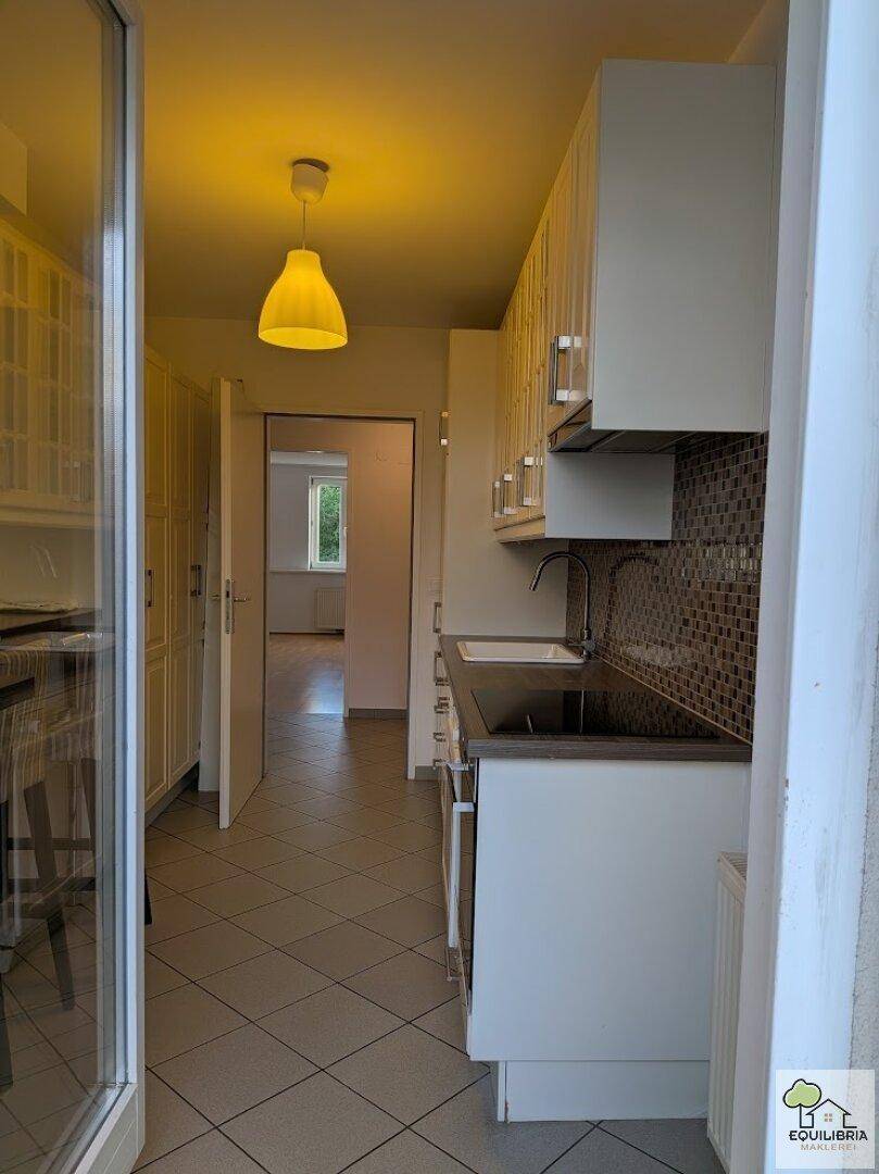Blick vom Balkon in die Küche mit weißen Schränken, Fliesenboden und Durchgang zu weiteren Räumen.