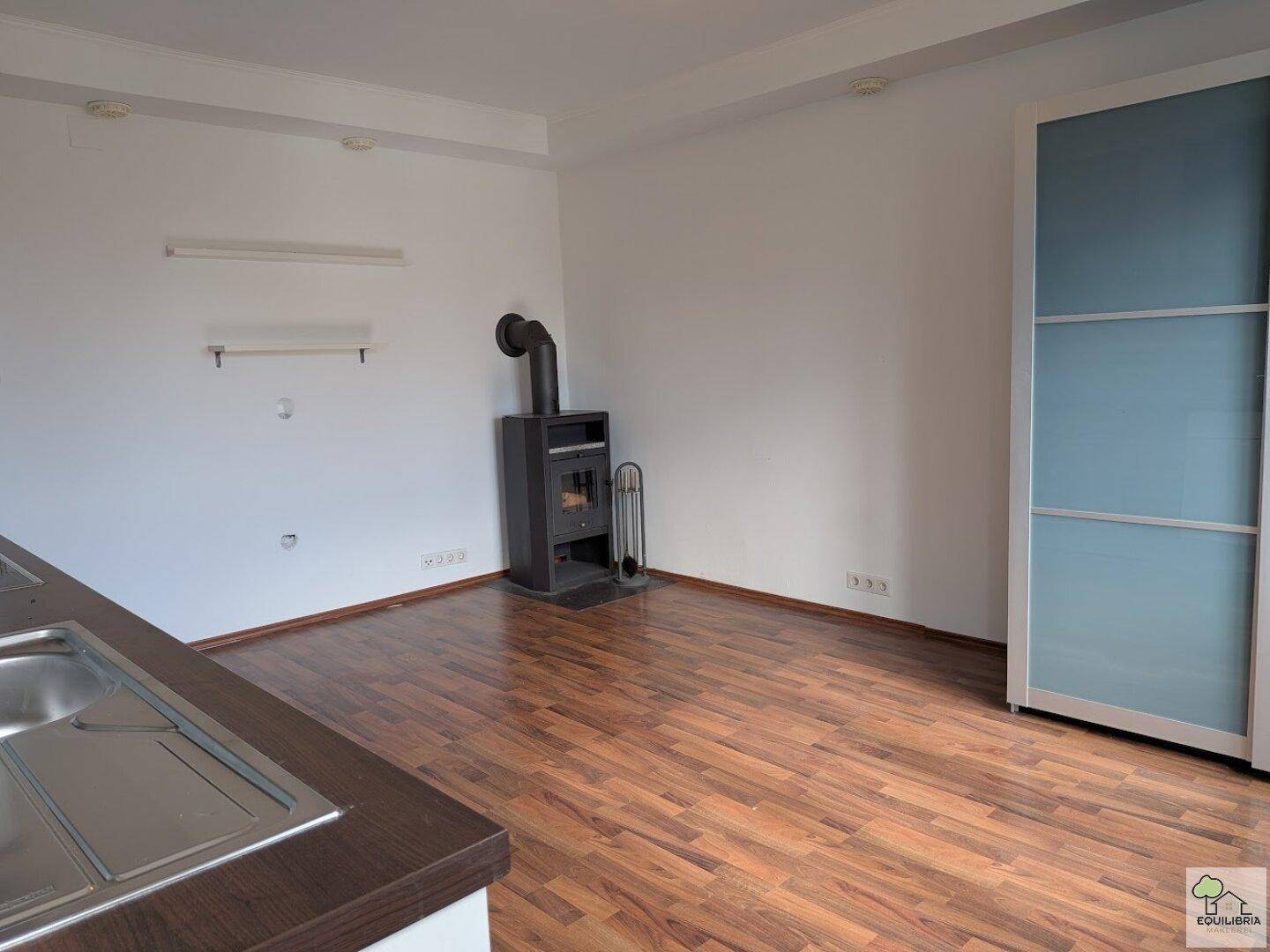 Offener Wohnbereich mit Kaminofen, Holzboden und einem modernen Kleiderschrank.