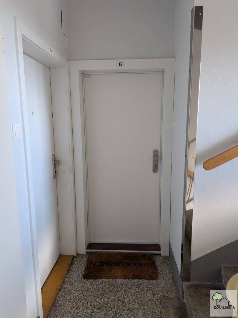 Eingangsbereich einer Wohnung mit heller Tür und Fußmatte auf Terrazzoboden.