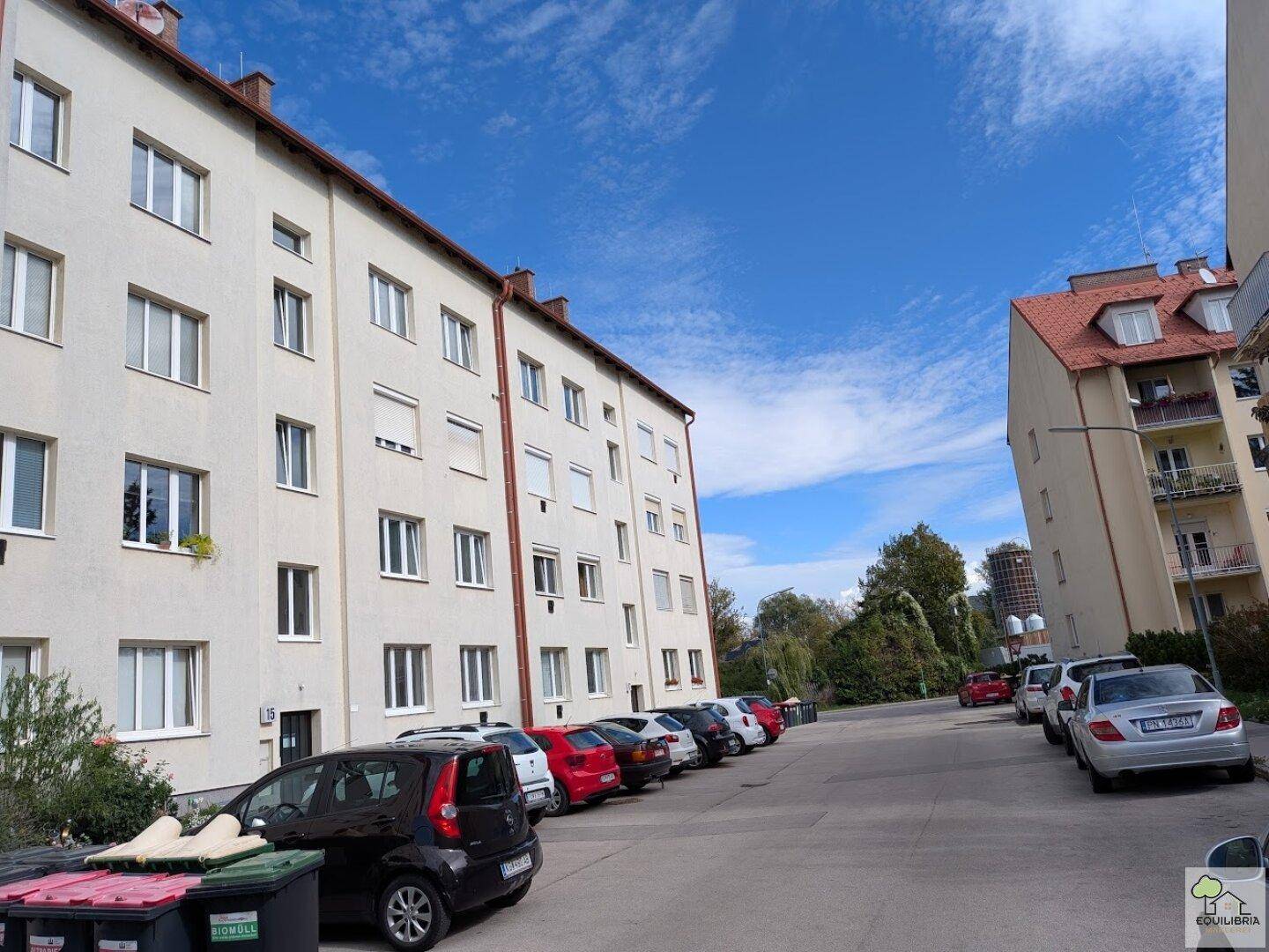 Mehrfamilienhaus mit mehreren Etagen und parkenden Autos entlang der Straße.