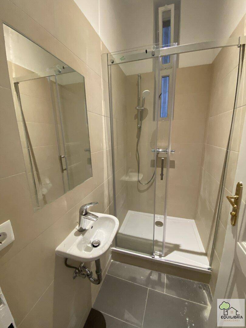 Modernes Badezimmer mit Duschkabine, Waschbecken und beigen Wandfliesen.