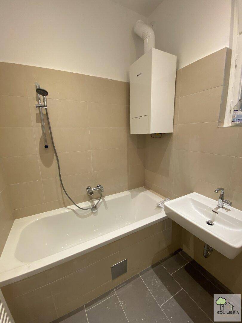 Badezimmer mit Badewanne, Waschbecken und Gastherme, hell gefliest.