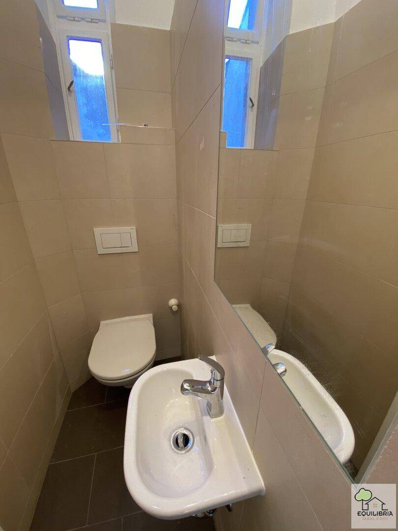 Modernes Gäste-WC mit beigen Fliesen, wandhängender Toilette und kleinem Waschbecken.