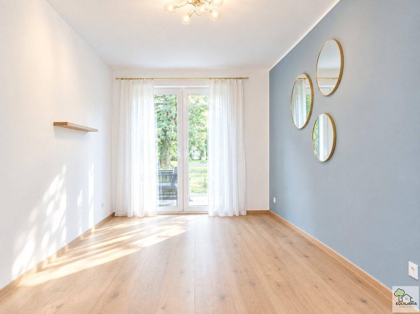 Helles Wohnzimmer mit Holzboden, blauer Akzentwand und Zugang zu einem Außenbereich.