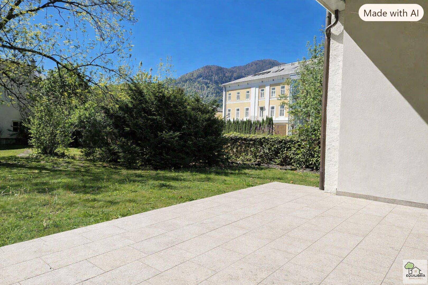 Sonniger Außenbereich mit gepflasterter Terrasse, Rasenfläche und Blick auf die Berge.