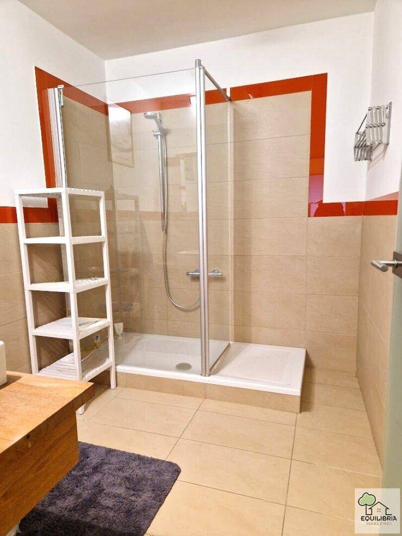 Badezimmer mit Duschkabine, beigefarbenen Fliesen und orangefarbenen Akzenten.