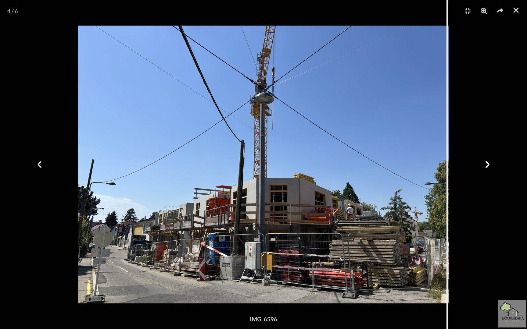 Baustelle mit einem großen Kran, Gerüsten und Baumaterialien an einer Straße unter blauem Himmel.