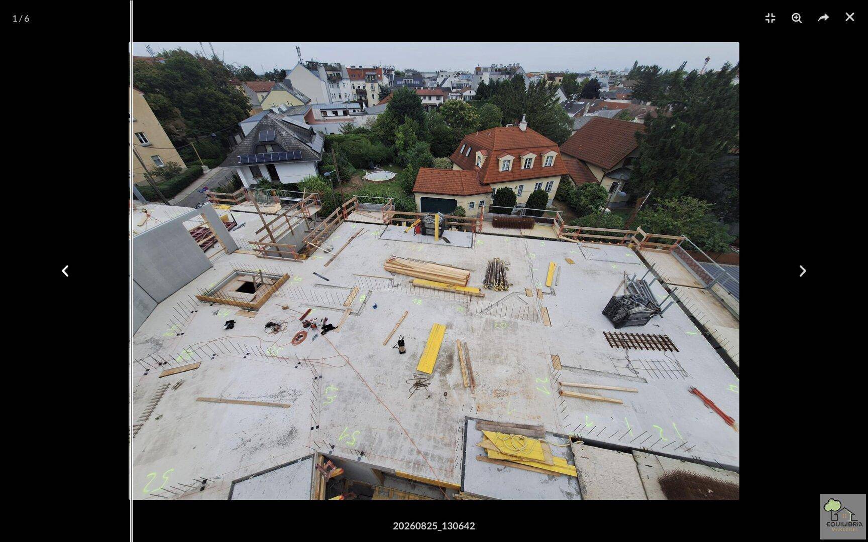 Baustellenansicht von oben mit Betonflächen, Baumaterialien und umliegenden Dächern.