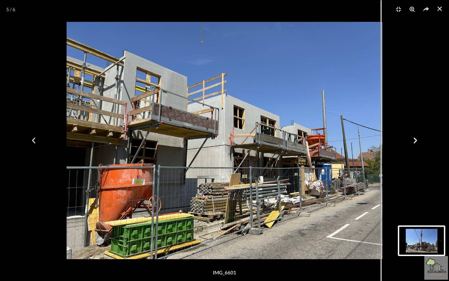 Baustellenansicht mit im Bau befindlicher Betonstruktur, Gerüsten und Baumaterialien am Straßenrand.