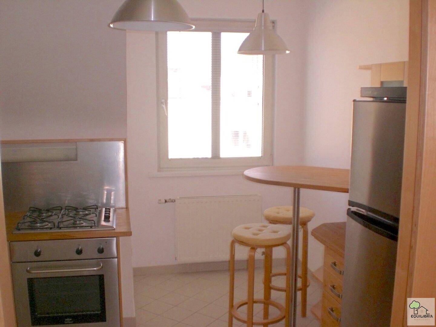 Funktionale Küche mit Gasherd, Backofen und Essbereich mit Barhockern am Fenster.