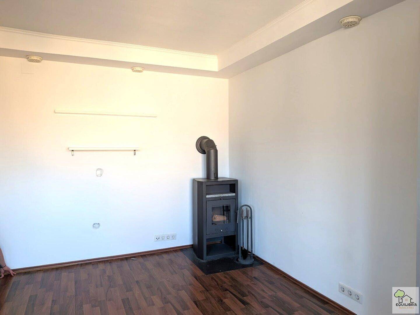 Heller Wohnraum mit Holzboden und einem modernen Holzofen in der Ecke, bereit für gemütliche Abende.