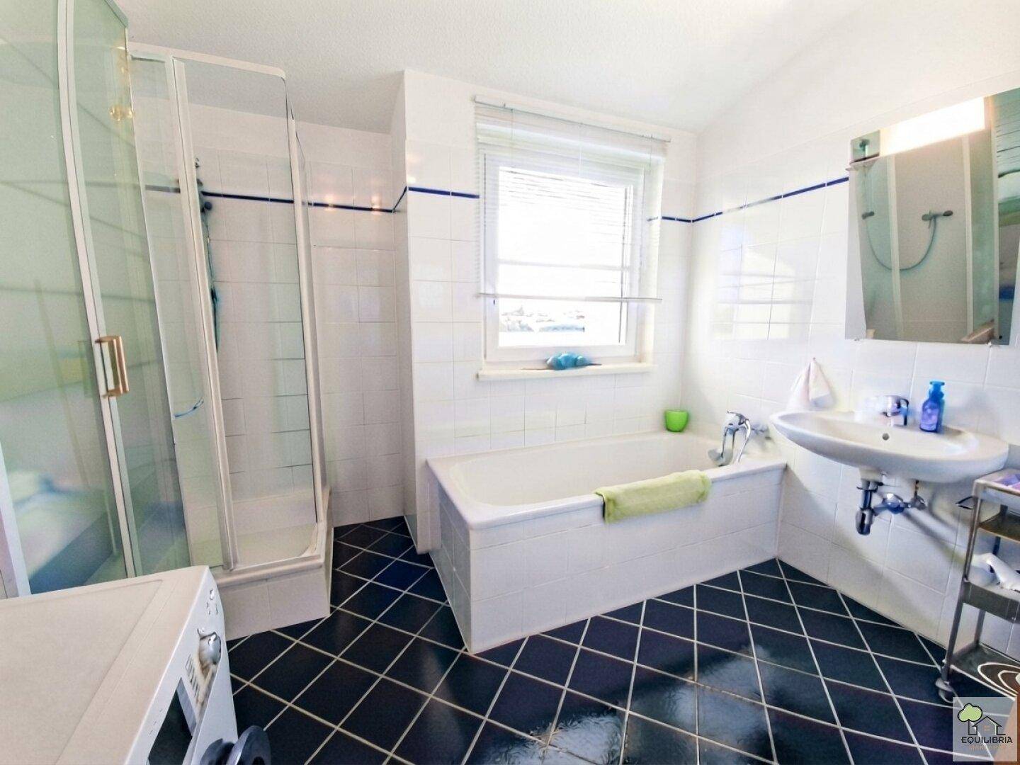 Badezimmer mit Badewanne, Duschkabine, Waschbecken und Fenster, ausgestattet mit Waschmaschine.