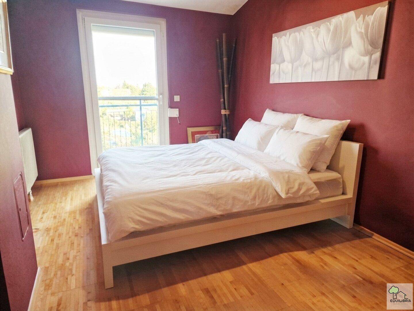 Gemütliches Schlafzimmer mit roter Wandfarbe, weißem Bett und direktem Balkonzugang.