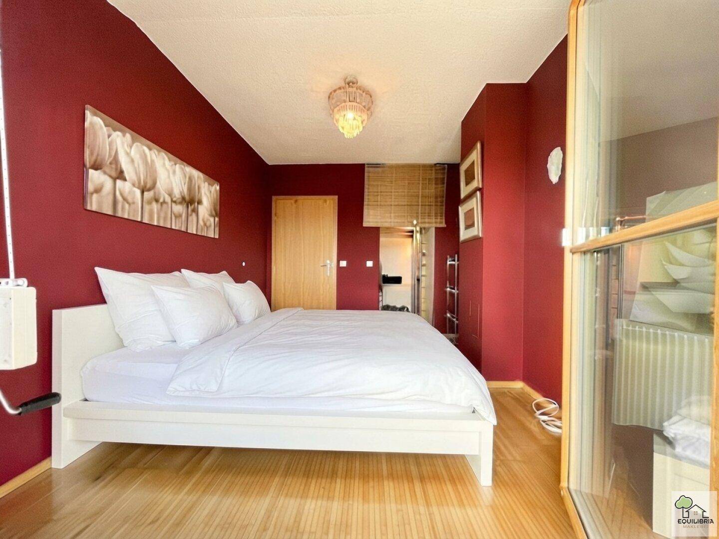 Schlafzimmer mit Holzboden, roter Wandgestaltung und einem großen Bett.