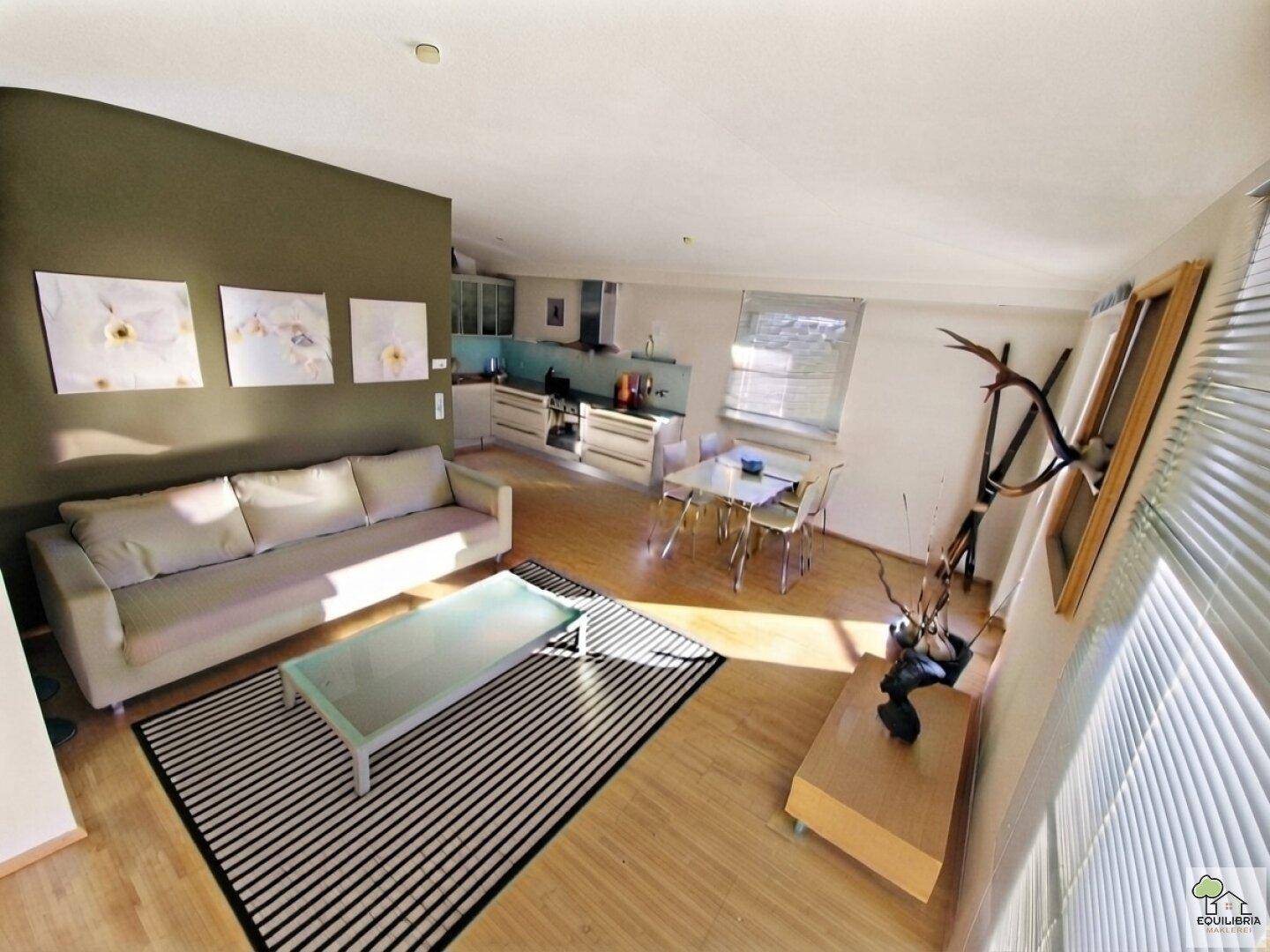 Lichtdurchfluteter Wohnbereich mit Parkettboden, beiger Couch und Blick auf die offene Küche.