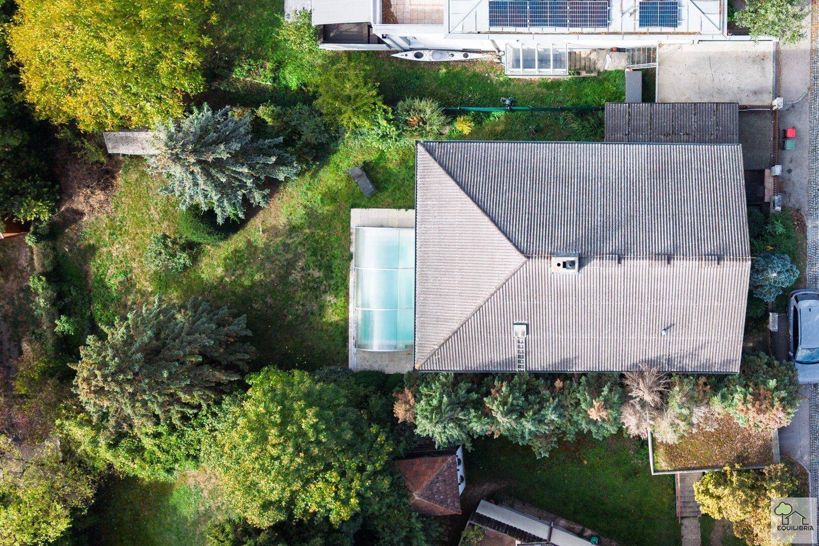 Draufsicht auf das Haus mit Satteldach, Garten, Pool und angrenzender Straße.