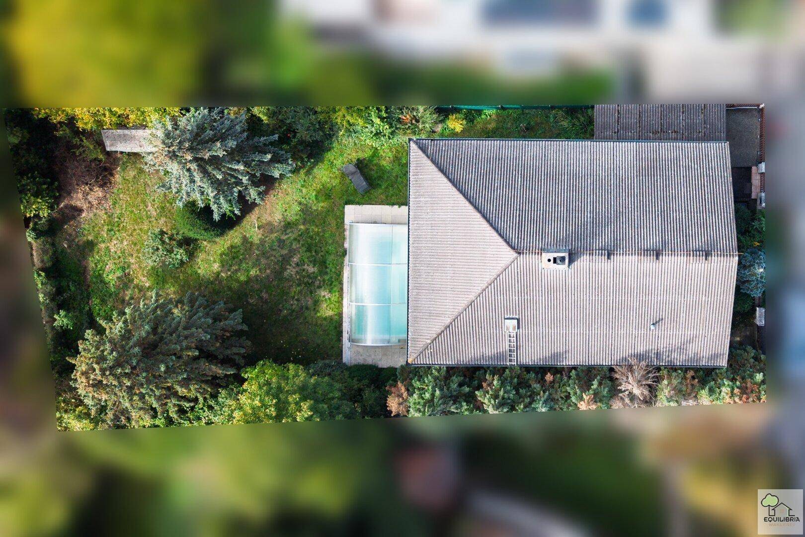 Vogelperspektive des Hauses mit Garten, überdachtem Pool und umgebender Vegetation.