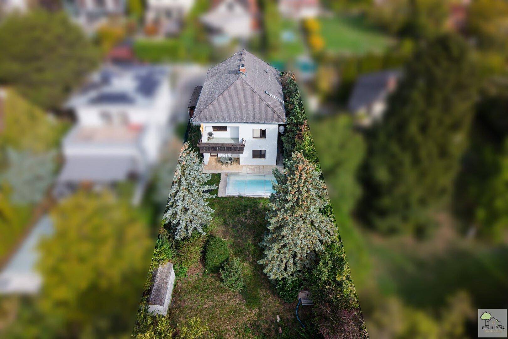 Luftaufnahme des Anwesens mit Haus, Garten und Pool, eingebettet in eine grüne Umgebung.