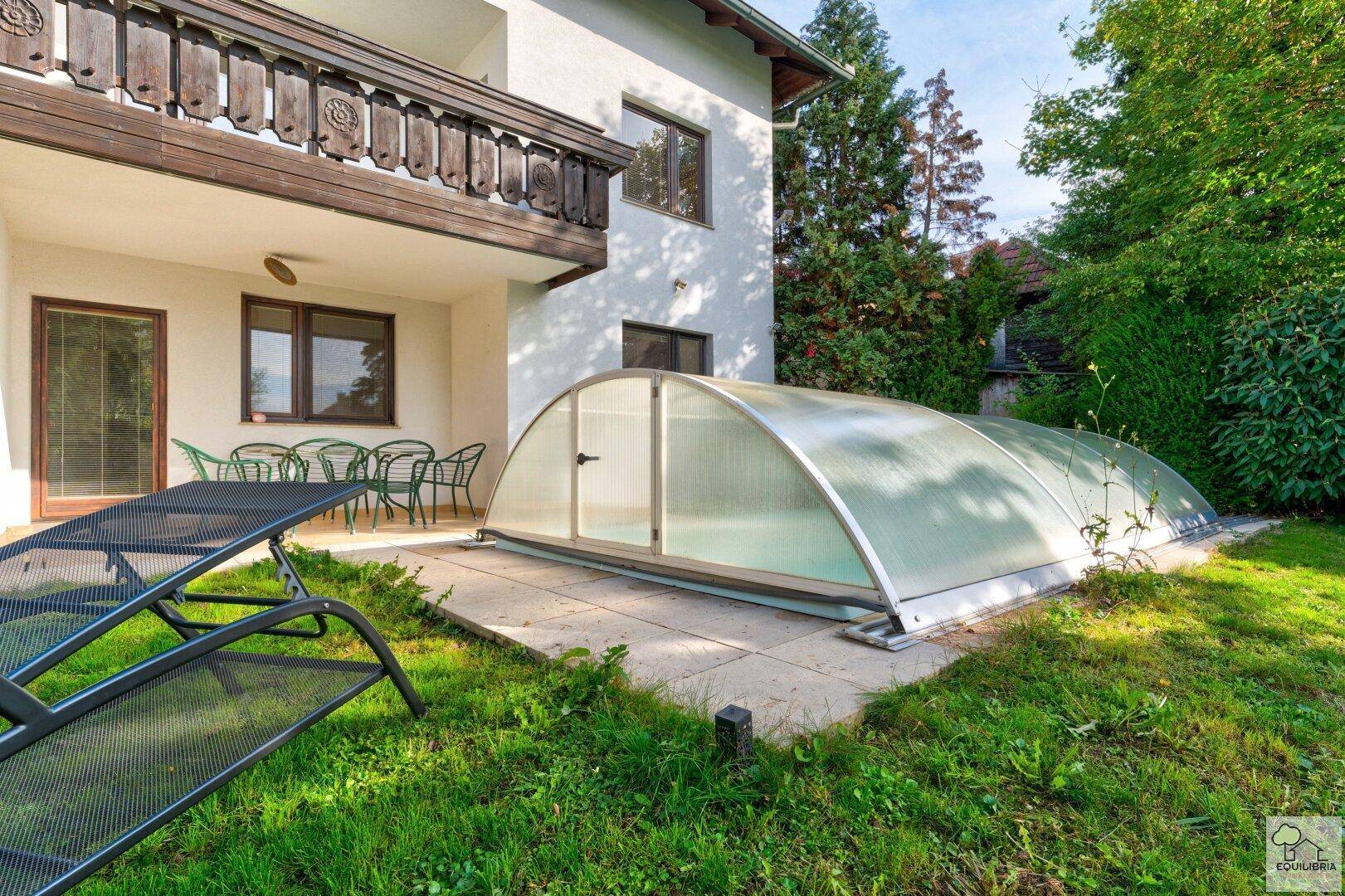 Entspannungsbereich auf der Terrasse mit Sonnenliege und Blick auf den überdachten Pool.