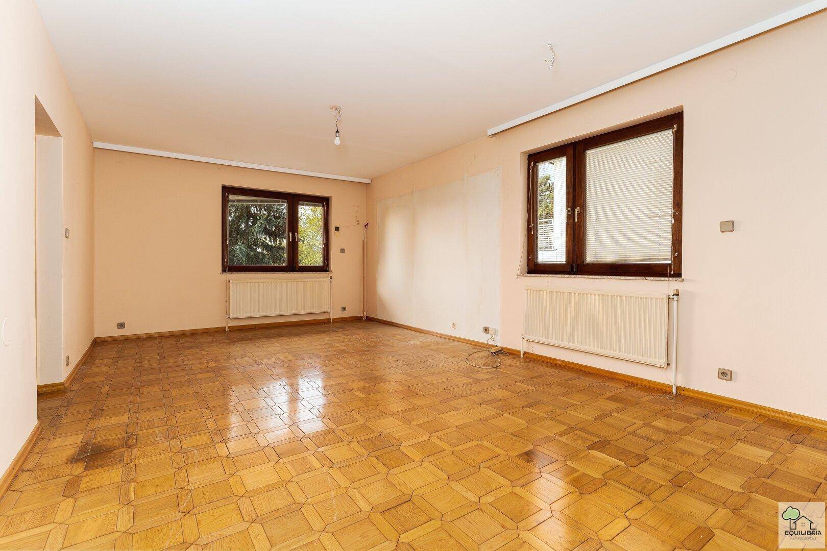 Geräumiges Wohnzimmer mit Parkettboden und zwei Fenstern, bereit zur individuellen Gestaltung.