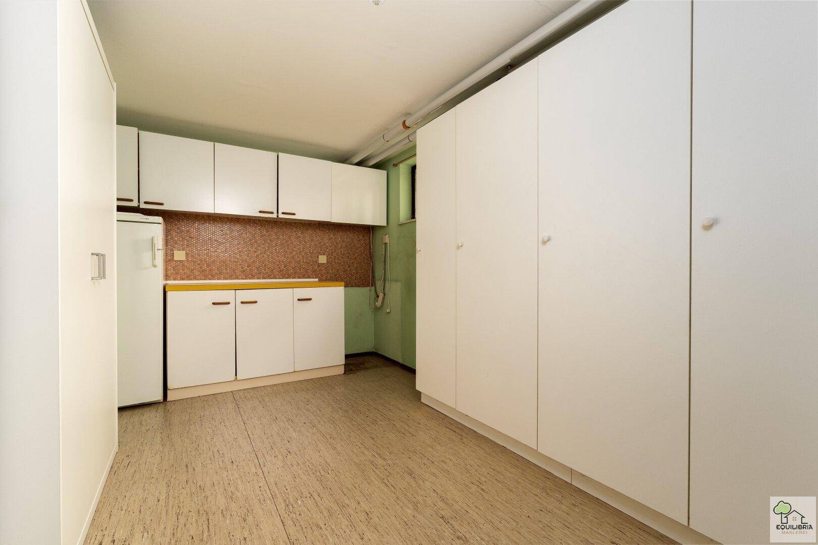 Praktischer Hauswirtschaftsraum mit viel Stauraum, Schränken und einem Kühlschrank.