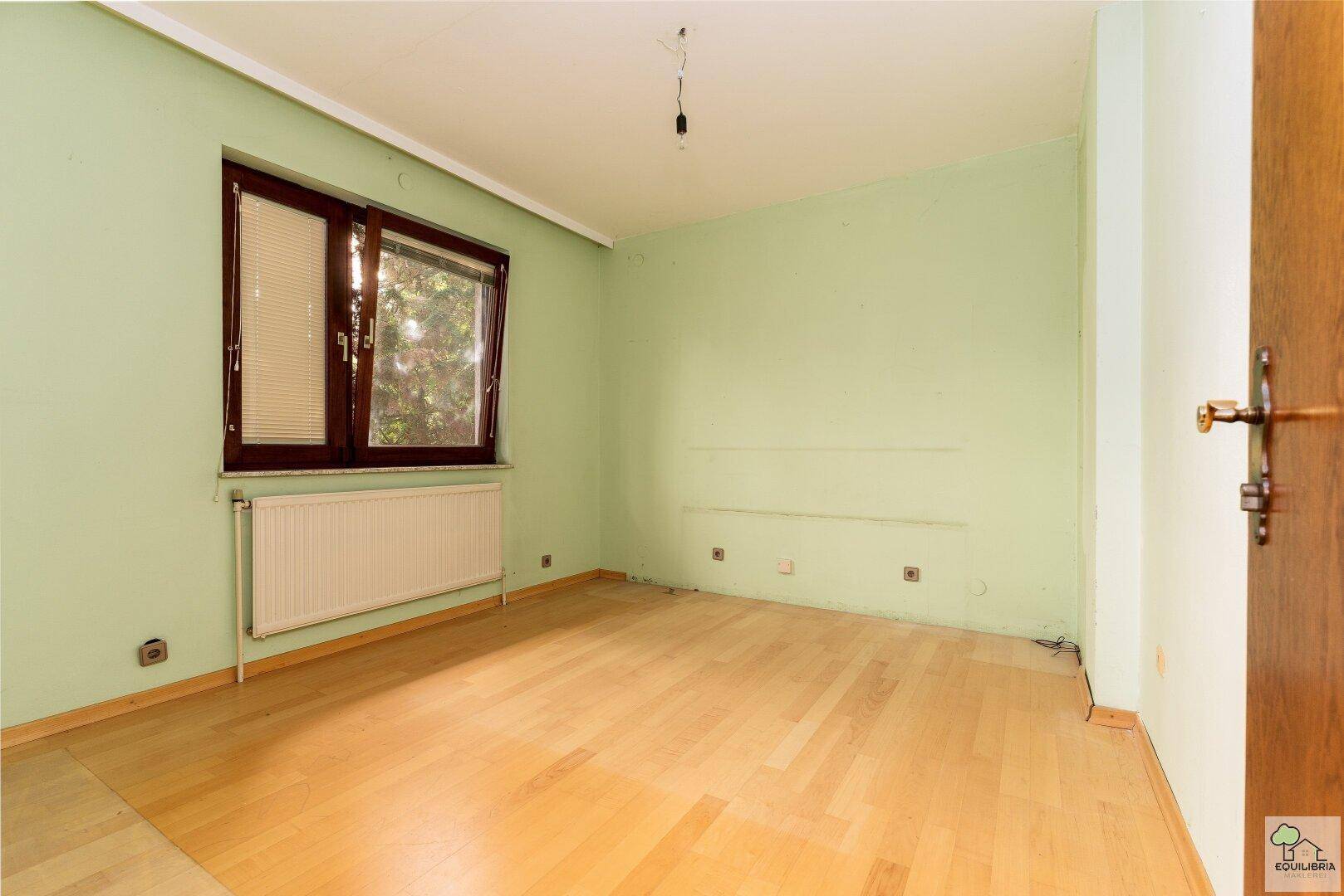 Helles Schlafzimmer mit hellem Holzboden und Fenster mit Blick ins Grüne.