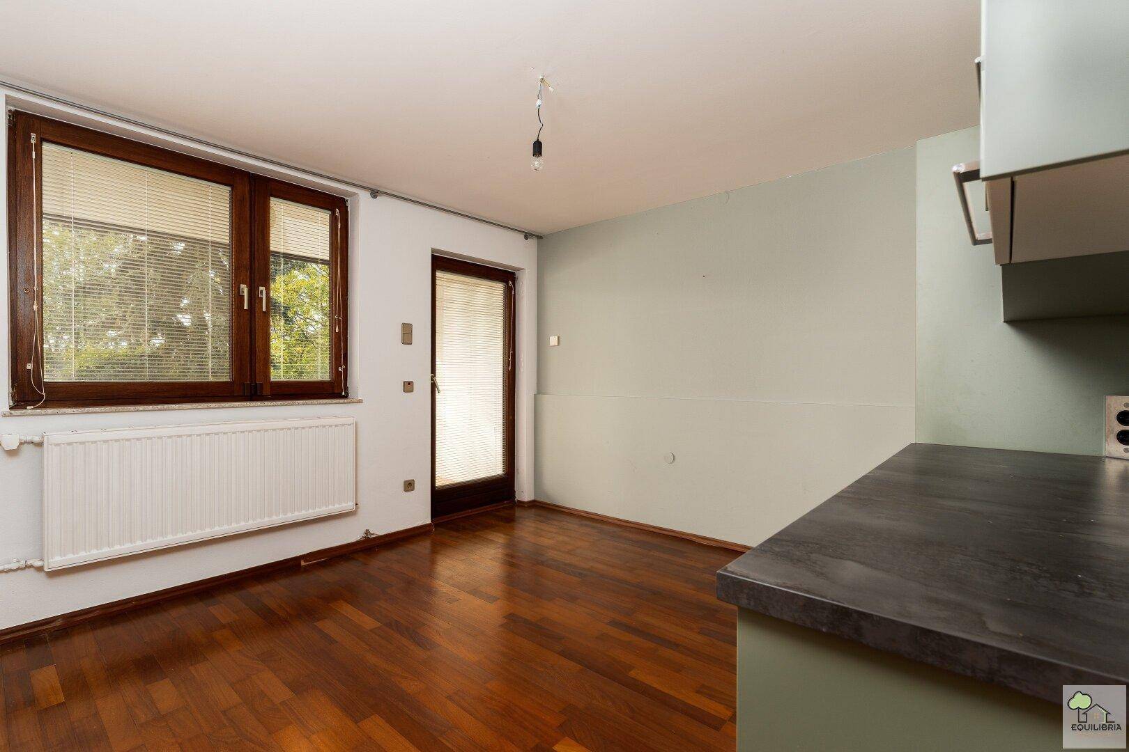 Heller Raum mit dunklem Holzboden und Zugang zu einem Außenbereich.