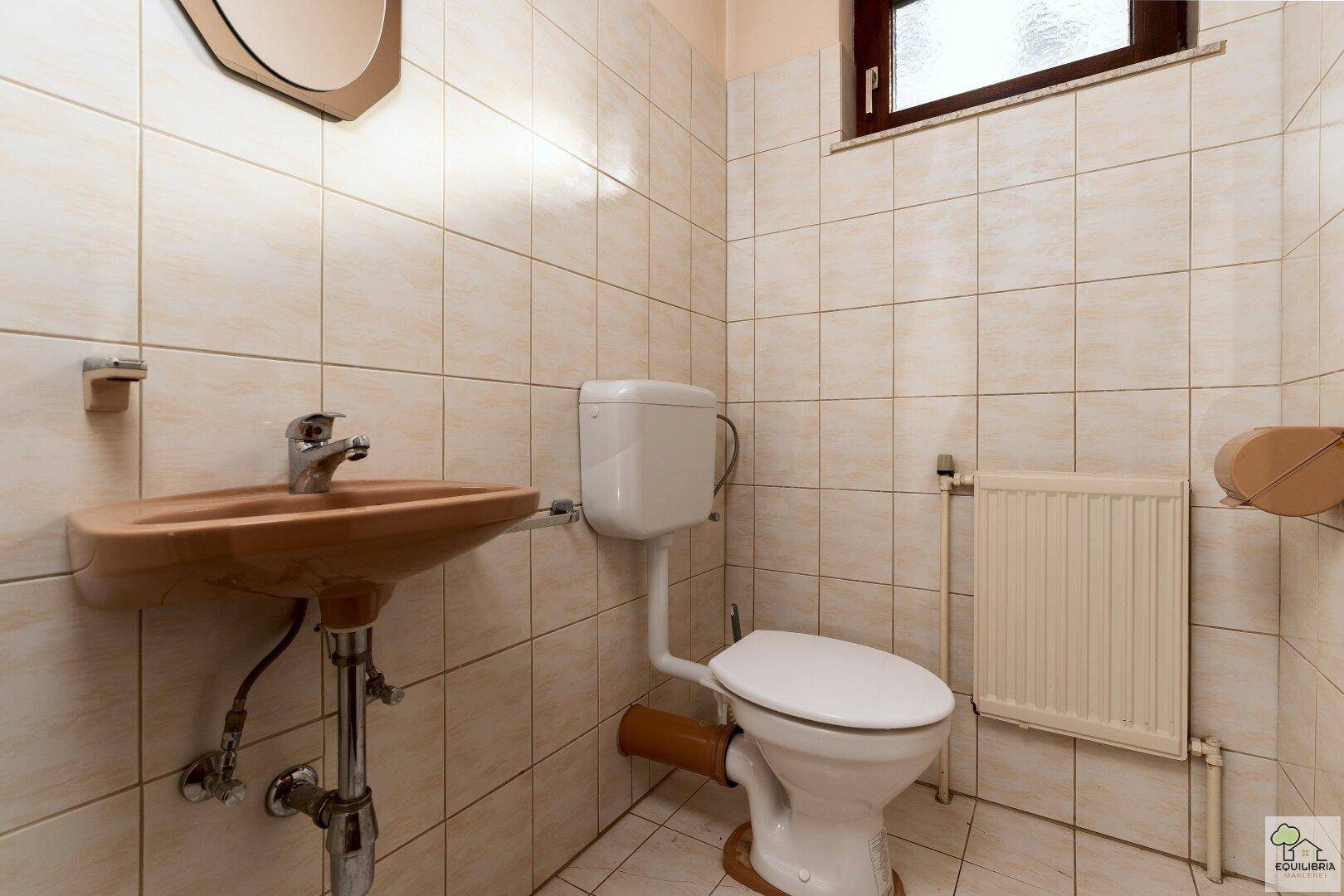 Kleines Gäste-WC mit Waschbecken, Toilette und Fenster.
