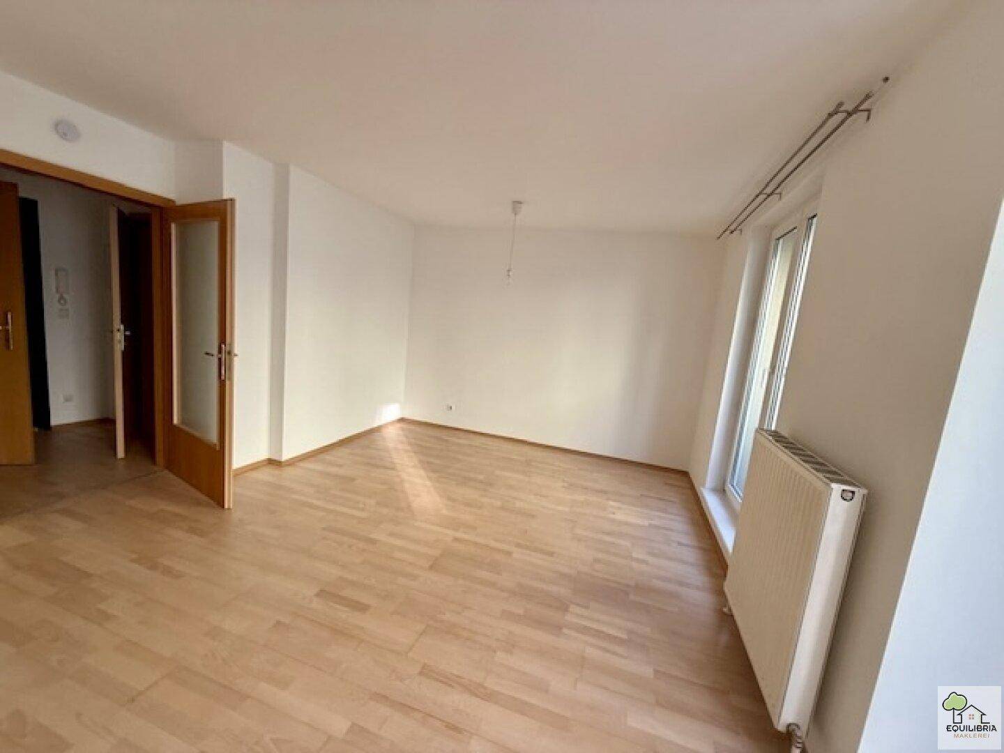 Geräumiges Wohnzimmer mit Holzboden, großem Fenster und Heizkörper, bietet viel Tageslicht.