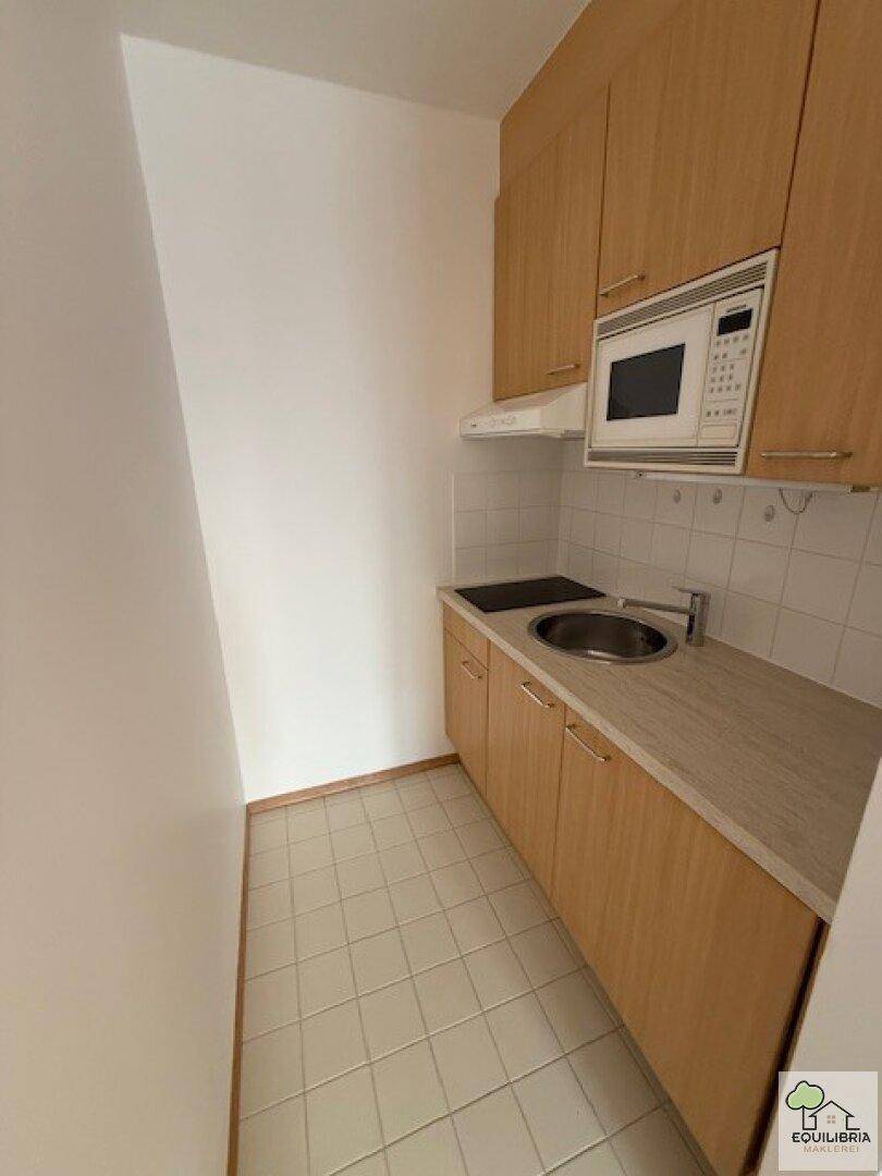 Schmale Küchenzeile mit Holzschränken, Spüle und Kochfeld, ergänzt durch einen Fliesenboden.