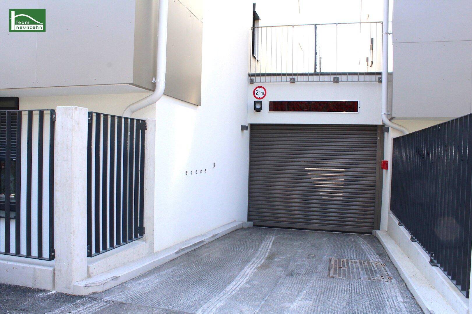 Einfahrt zur Tiefgarage mit Rolltor und moderner Gebäudearchitektur.