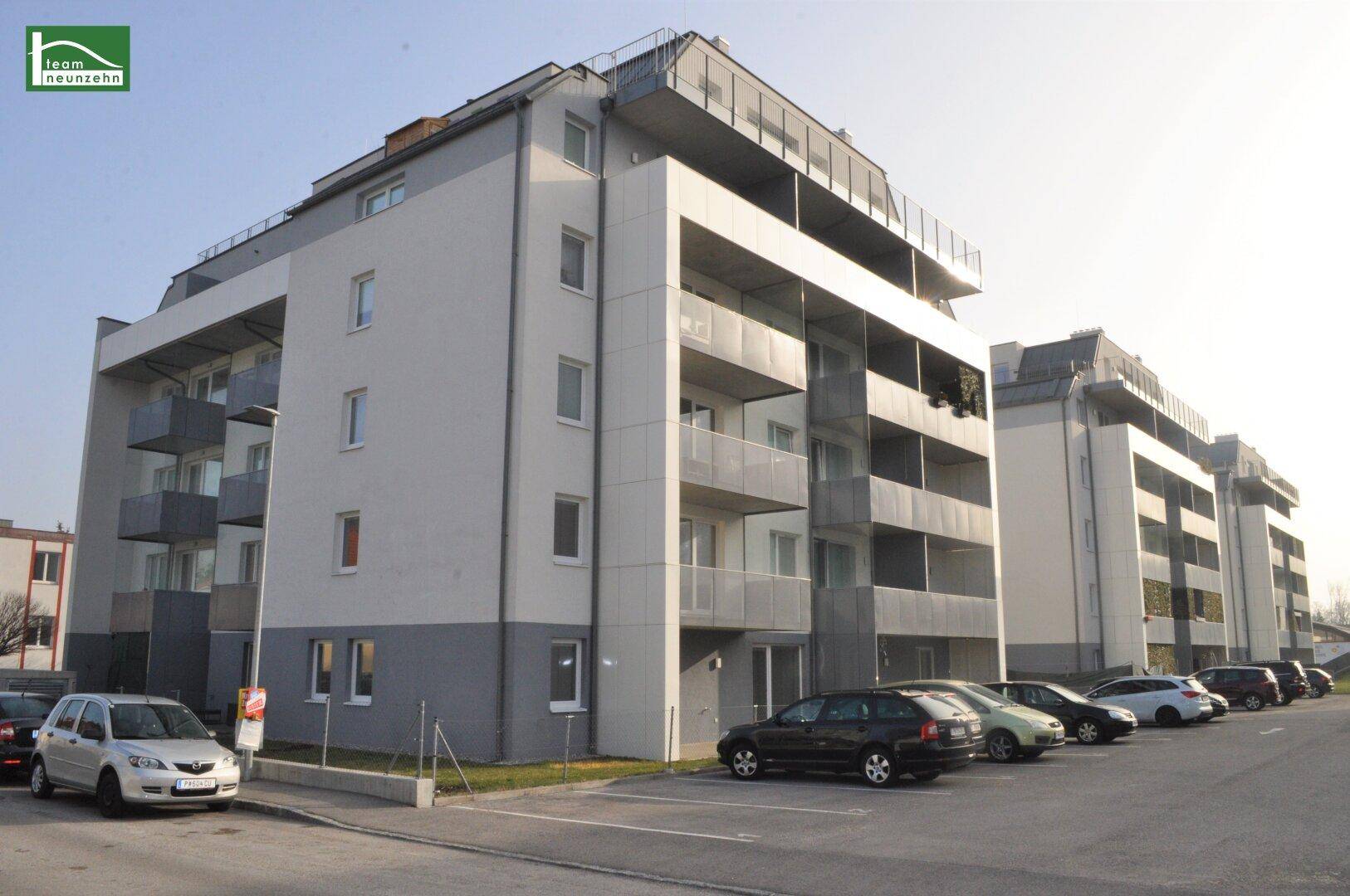 Modernes Mehrfamilienhaus mit Balkonen und Außenstellplätzen unter klarem Himmel.