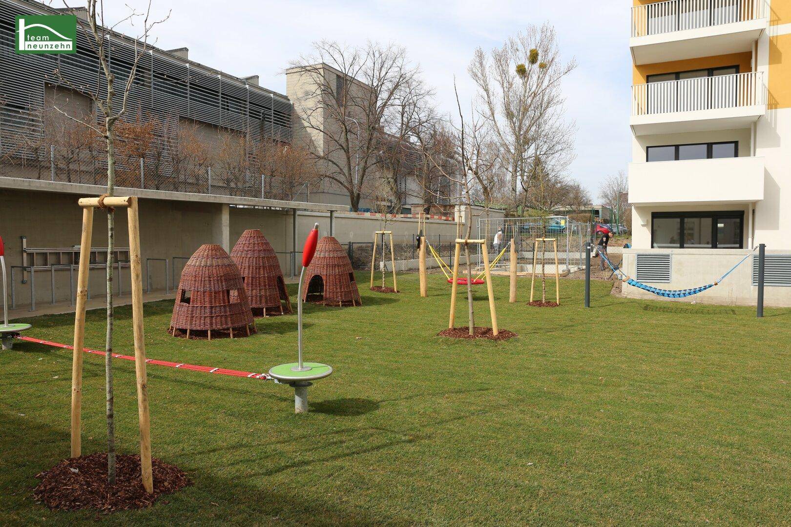 Grüner Spielplatzbereich mit verschiedenen Spielgeräten und einer Hängematte.