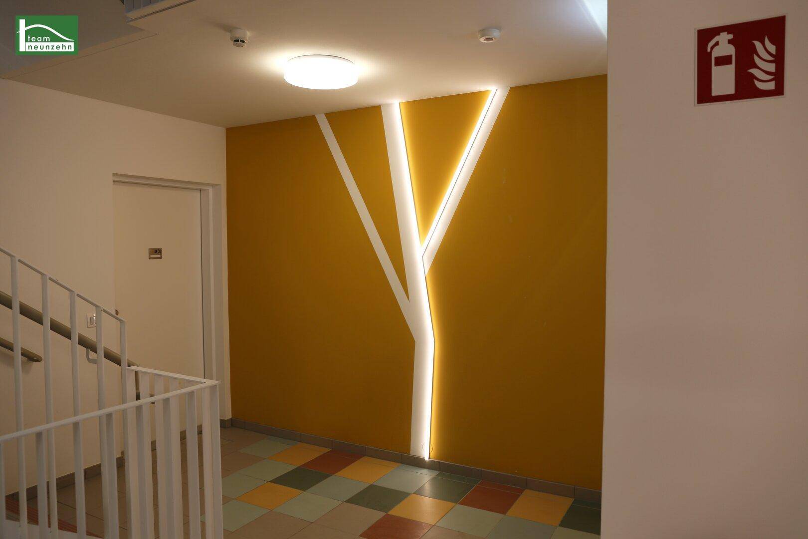 Moderner Eingangsbereich mit künstlerischer Wandgestaltung und farbenfrohem Fliesenboden.