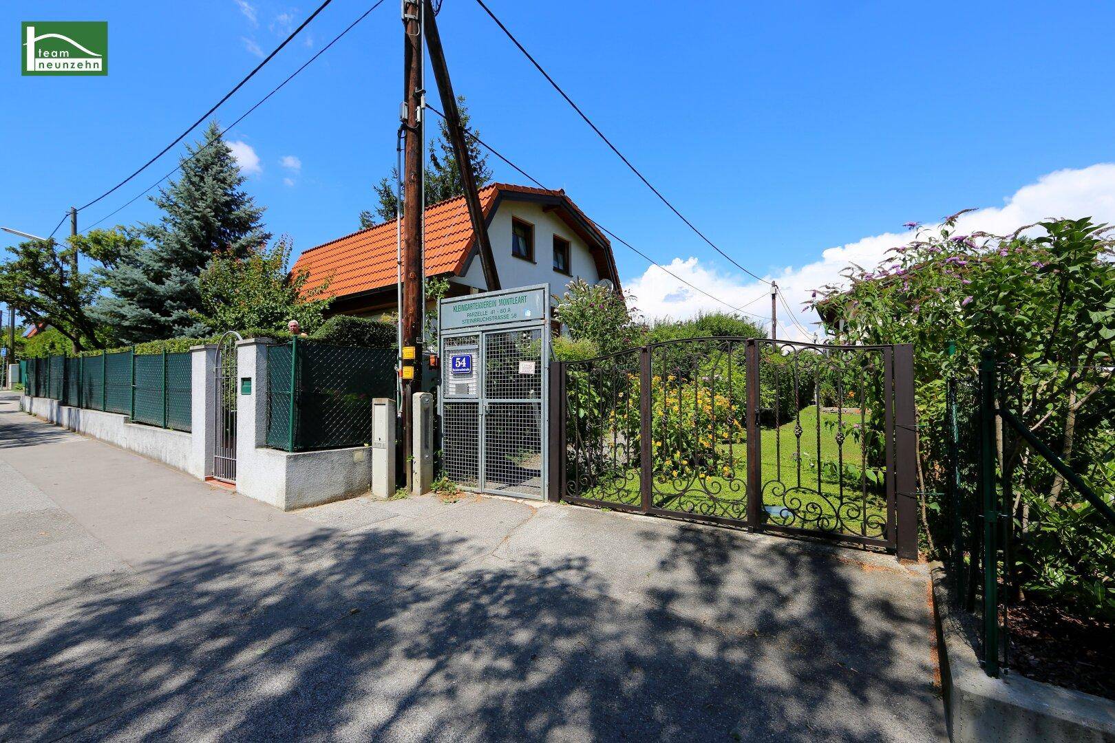 Eingangsbereich eines Grundstücks mit schmiedeeisernem Tor und grünem Garten.