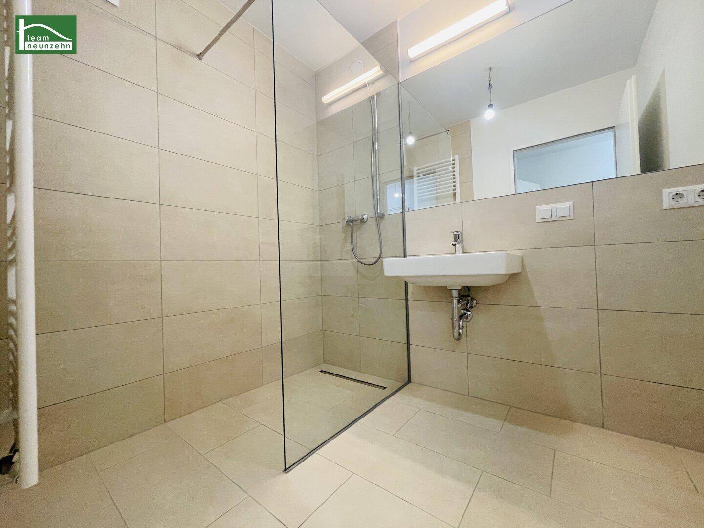 Modernes Badezimmer mit begehbarer Dusche, großem Spiegel und beigen Fliesen.