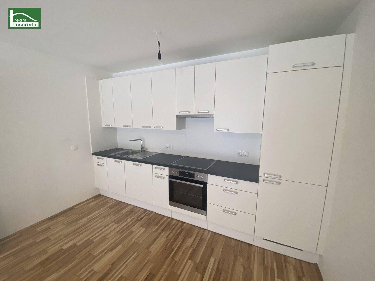 Moderne Einbauküche in Weiß mit dunkler Arbeitsplatte und integriertem Backofen.