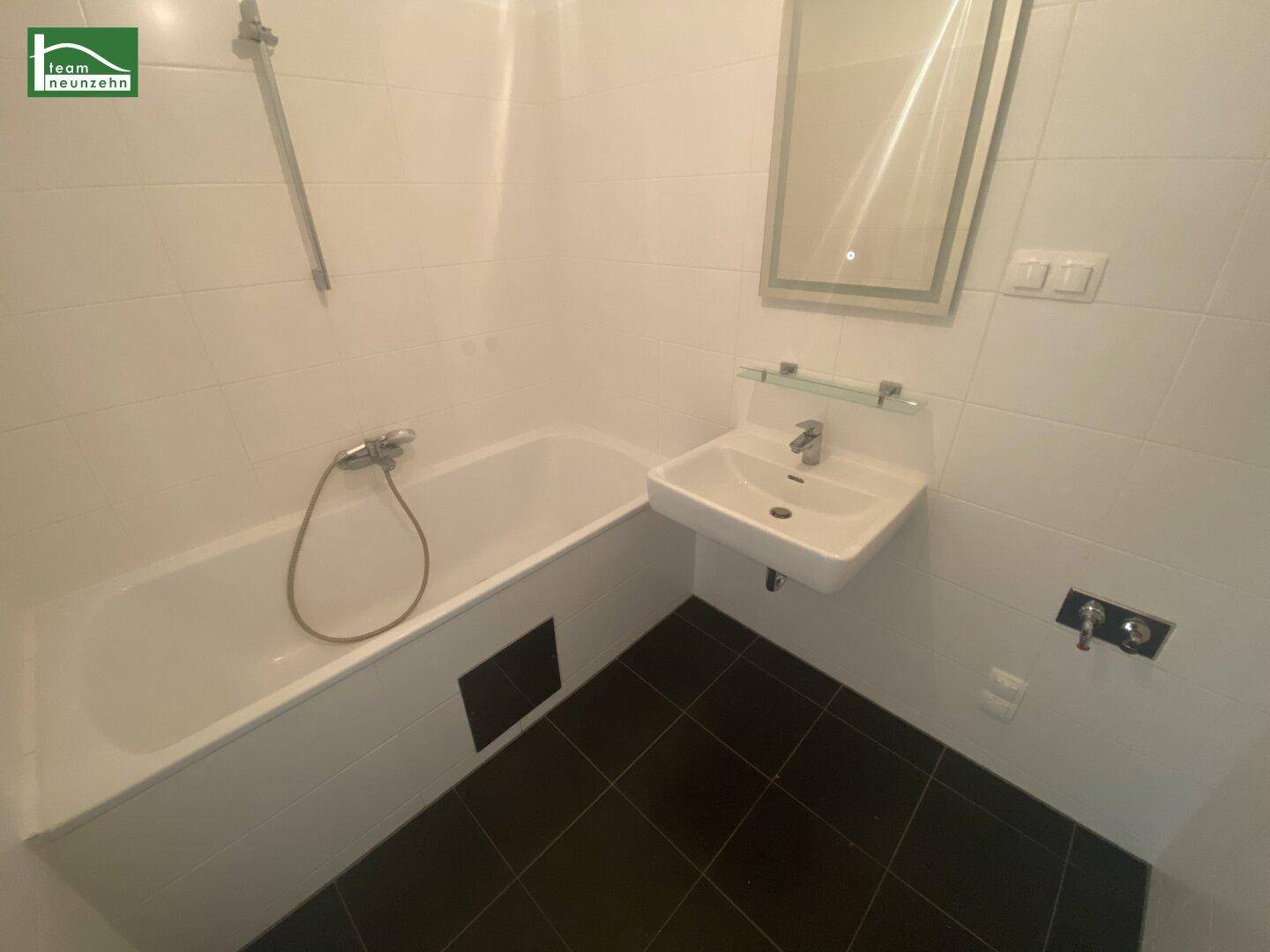 Funktionales Badezimmer mit Badewanne, Waschbecken und weißen Wandfliesen.
